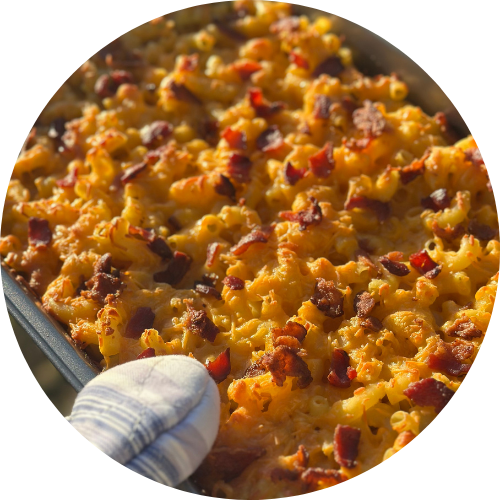 Mac n' cheese with bacon held by a hand with an oven mitt