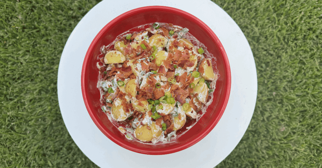Loaded up potato salad in red bowl.